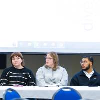 five college student panelists sitting at the front of a conference room, one speaking while the others listen